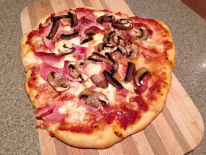 Cooked pizza with tomato sauce, mozzarella, ham, mushrooms.